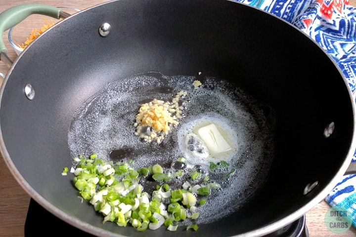 Garlic and chopped spring onions are sautéing in melted butter in a hot skillet.