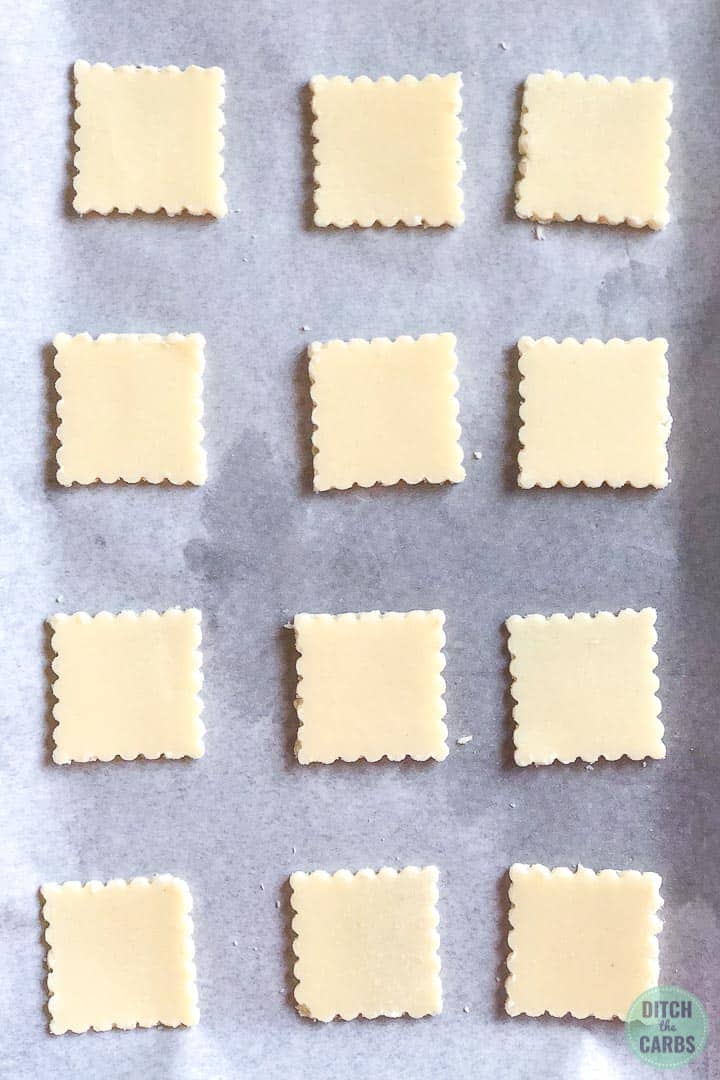 Keto shortbread cookie dough cut into squares with scalloped edges arranged in rows on a cookie sheet lined with parchment paper.