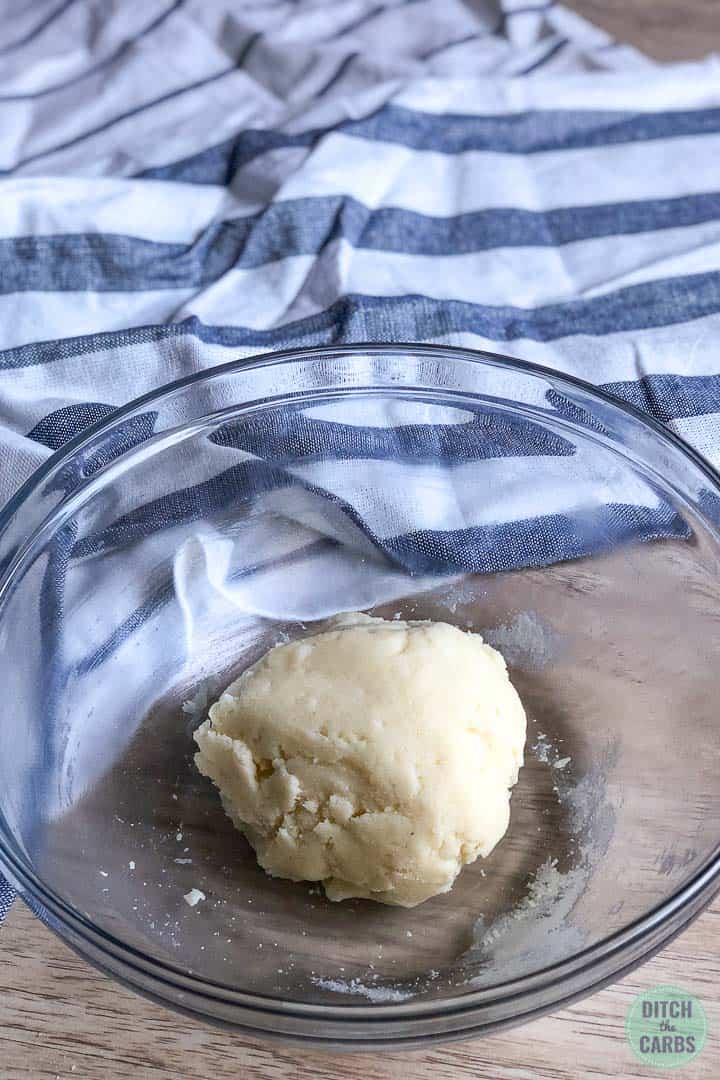 Masa para galletas de mantequilla prensada en una bola en un recipiente de vidrio transparente.
