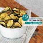 baked zucchini chips in a white bowl on a blue and white tea towel