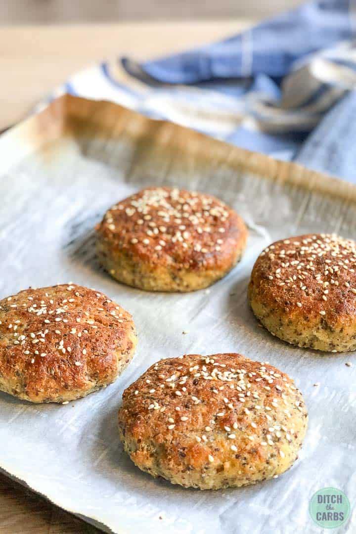 Four baked hamburger buns on a metal cookie sheet lined with white parchment paper.
