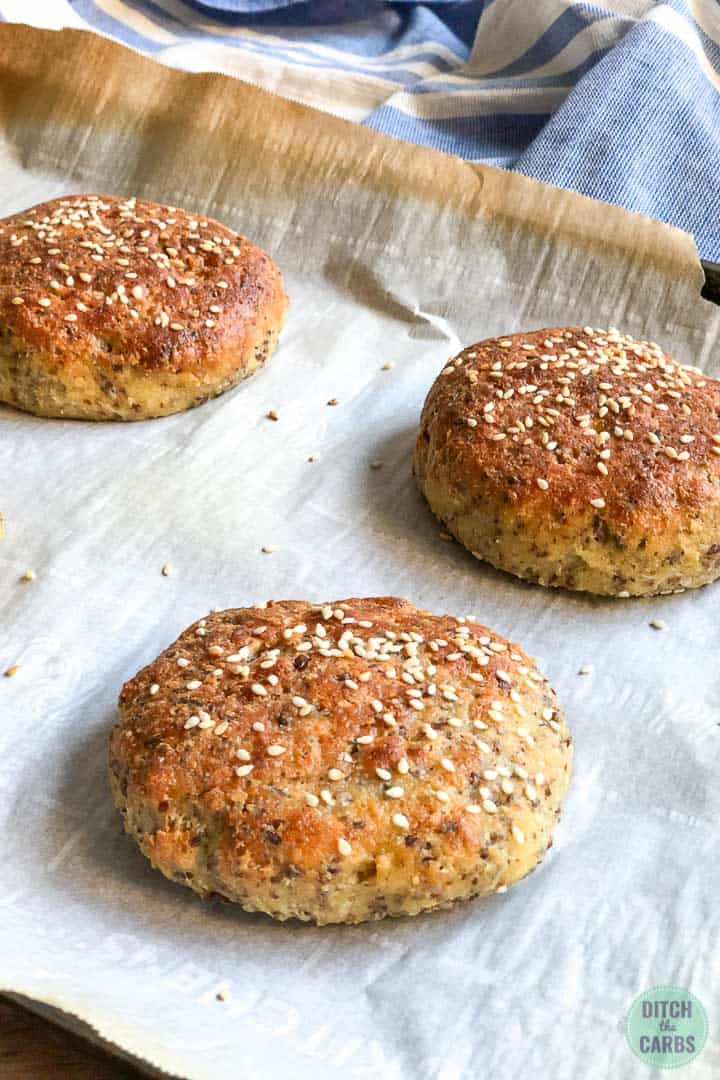 Baked keto hamburger buns on a metal cookie sheet lined with white parchment paper.