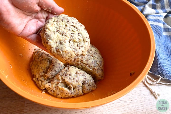 Mozzarella hamburger bun dough cut into four pieces. A hand is lifting and shaping one piece to form a bun.