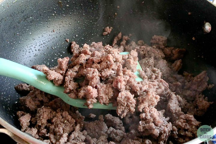 A light blue green spatula is lifting cooked ground beef out of a black skillet.
