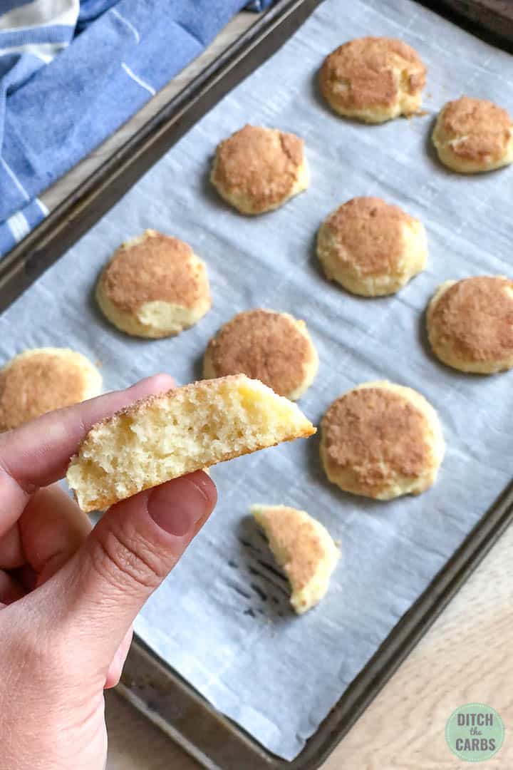 A hand is lifting a cooking from the cookies sheet of keto snickerdoodle cookies. The cookie has been broken in half to show how soft the cookies are.
