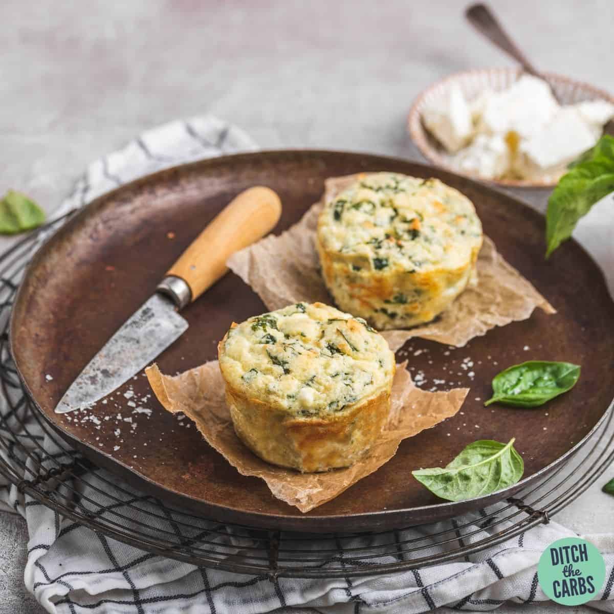 2 spinach and feta keto muffins on a dark pottery plate