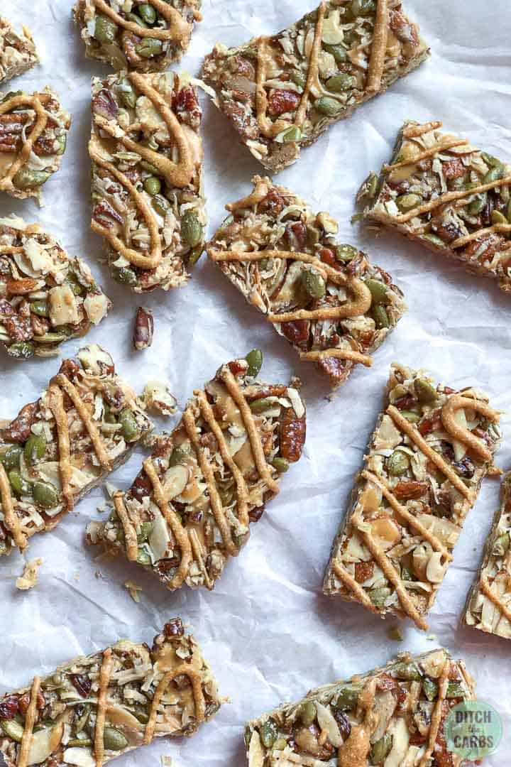 Keto peanut butter granola bars spread out over a pieces of white parchment paper.