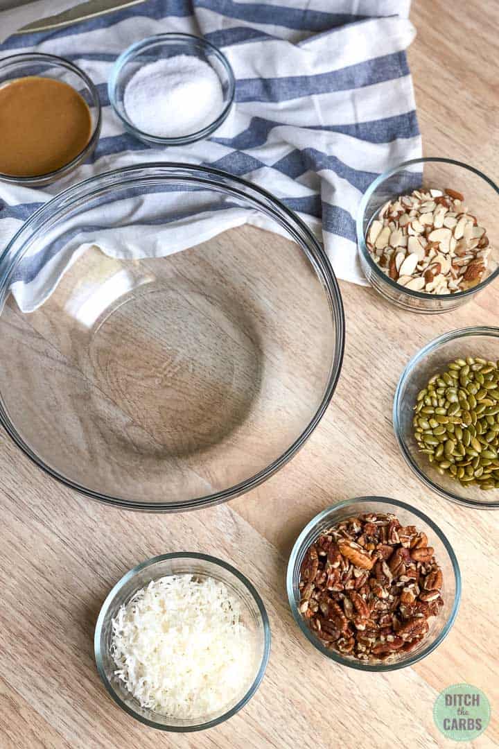 All the ingredients to make keto peanut butter granola bars are premeasured in clear glass bowls.
