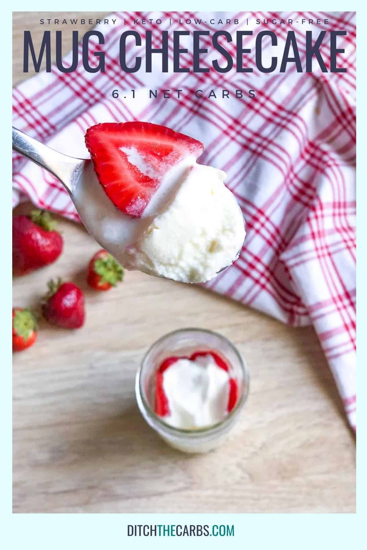 A spoon is lifting a bite of strawberry keto mug cheesecake from the cheesecake cooked in a clear glass jar. Strawberries are scatter on the table and a red checkered napkin is in the background.