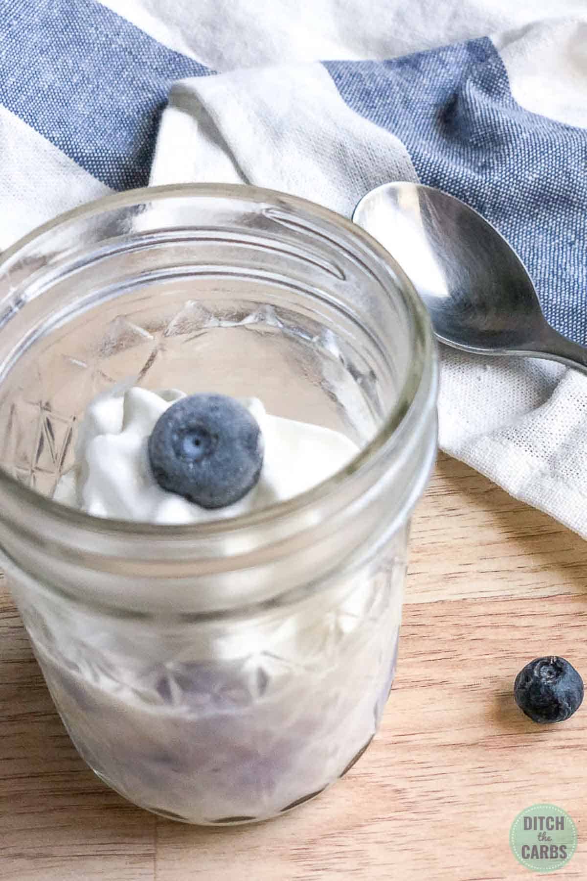 Cooked blueberry keto mug cheesecake is topped with whipped cream and a blueberry.
