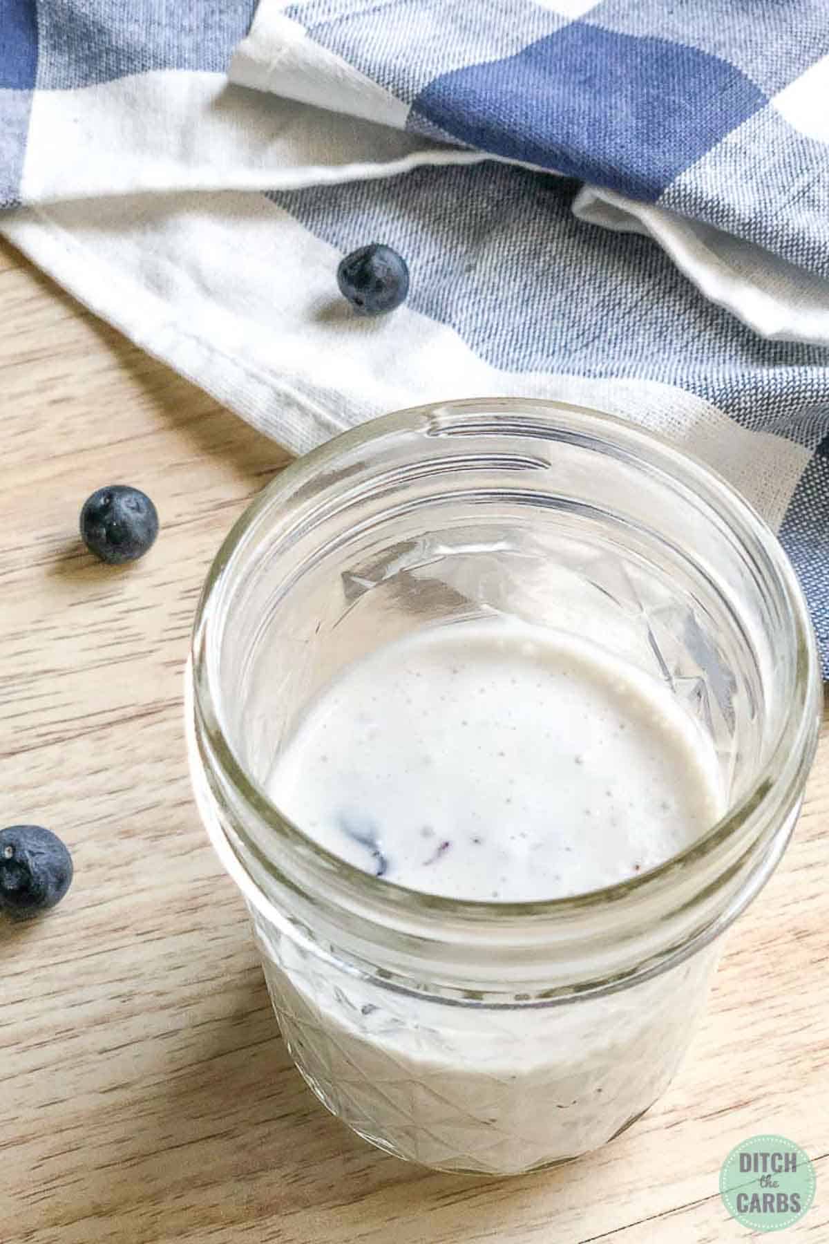 Blueberries have been smashed into the cheesecake batter in a clear glass jar. 