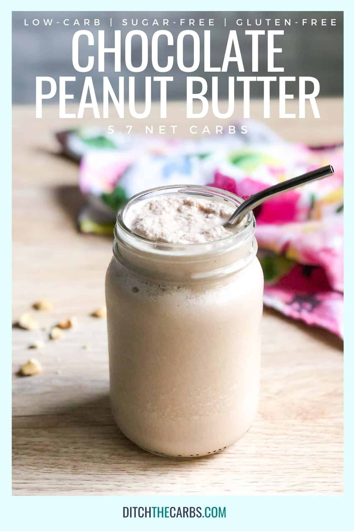 Keto chocolate peanut butter smoothie in a clear glass jar with a metal straw. Crushed peanuts are scattered in the background with a flower patterned towel.