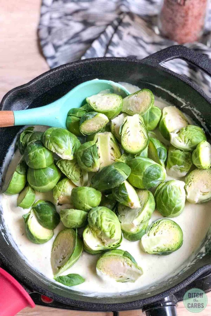 Creamy cheese sauce make in a skillet. The brussels sprouts have been cut in half and added to the skillet.