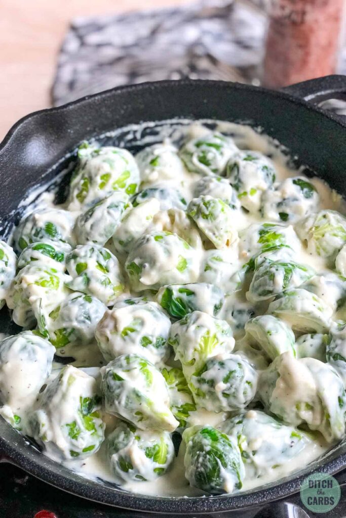 Brussels sprouts tossed in the cheese sauce in the skillet so that they are completed coated.