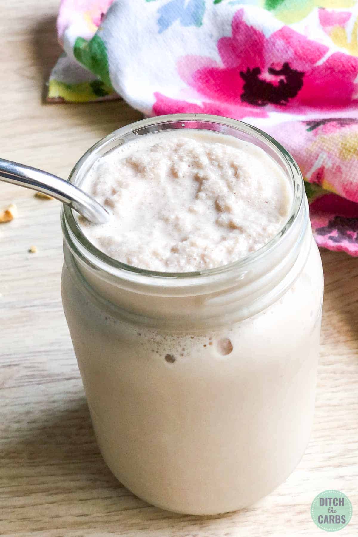 The keto chocolate peanut butter has been poured into a clear glass jar with a metal straw added to it.