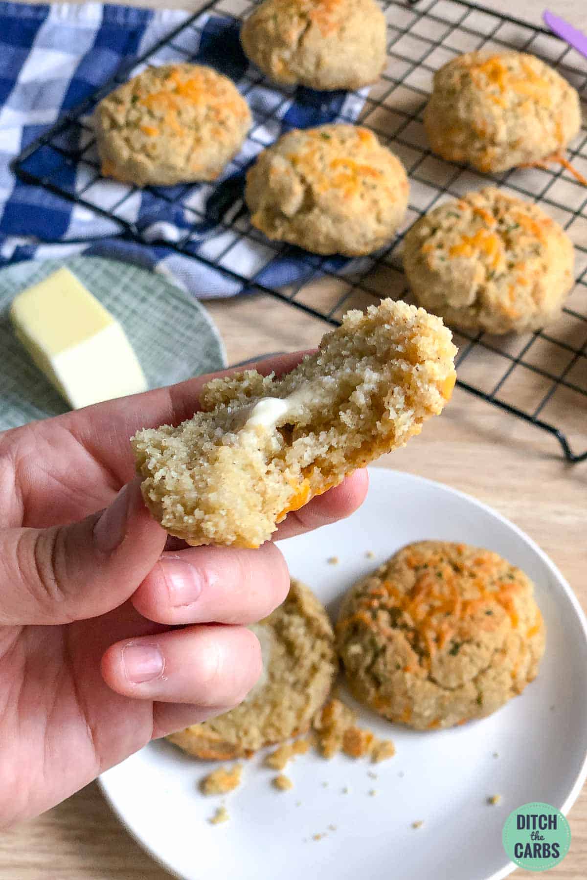 A hand lifting half a keto cheddar biscuit (scone) with a bite taken out of it.