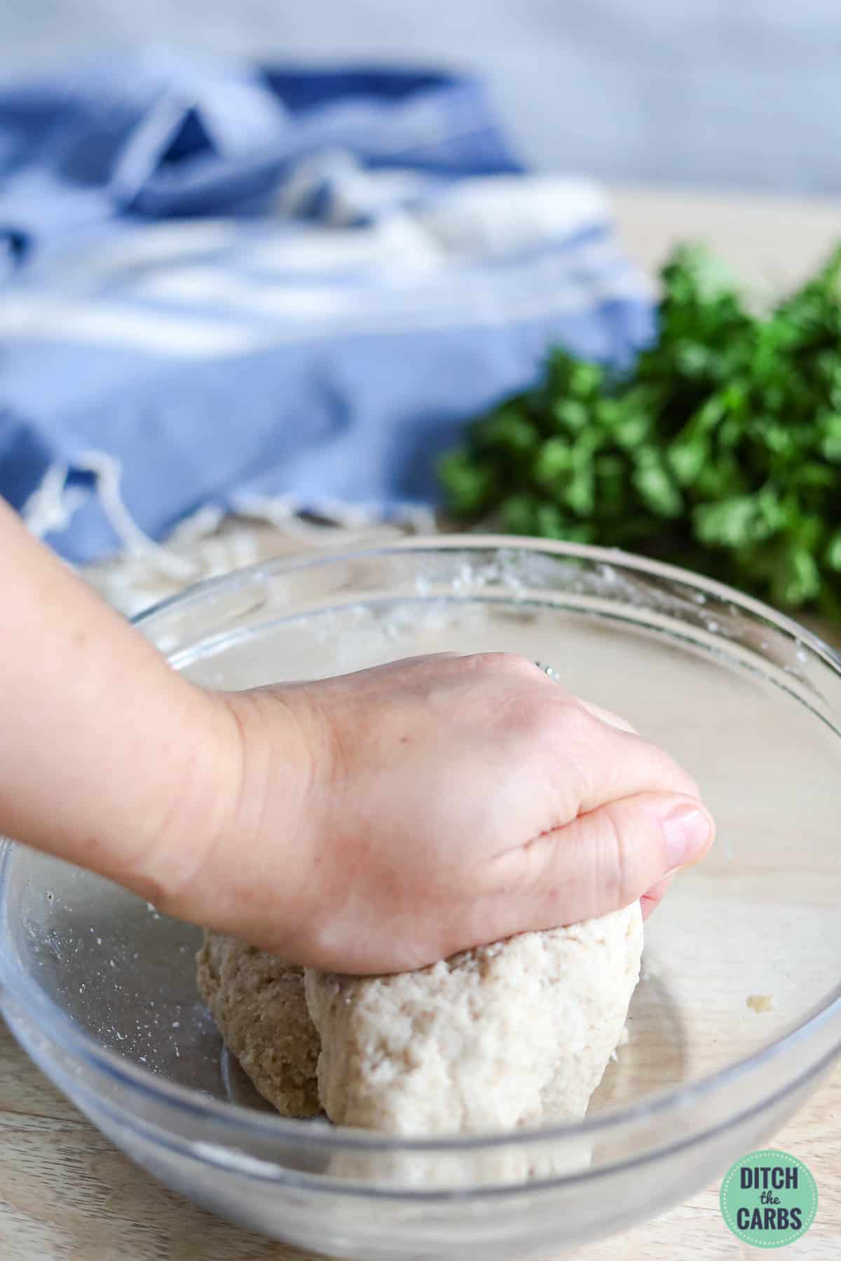 kneading roti dough by hand in a glass bowl