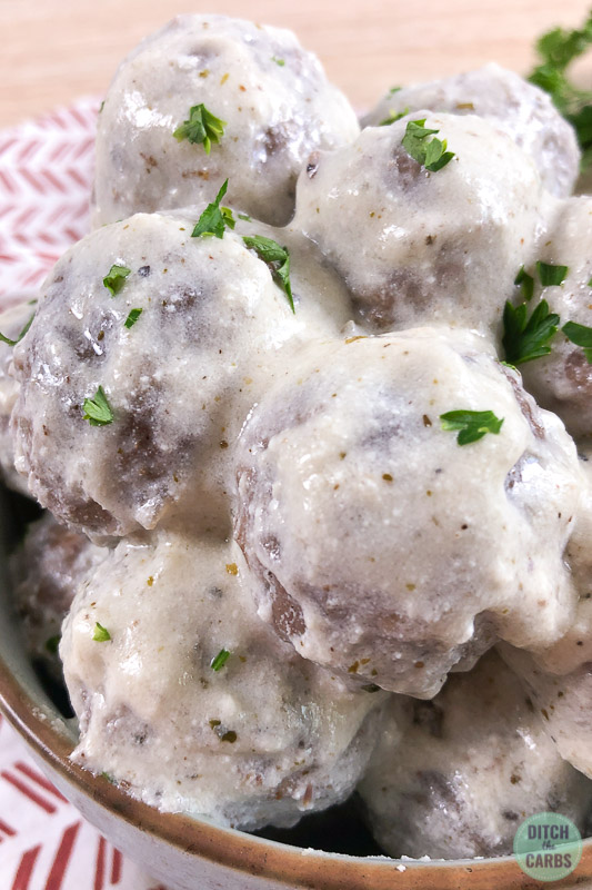 creamy meatballs covered in cheese sauce and chopped fresh herbs