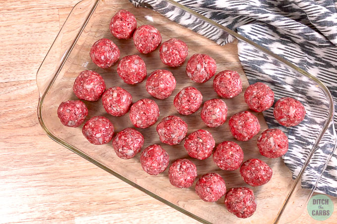 Keto meatballs shaped into balls and arranged in a clear glass baking pan.