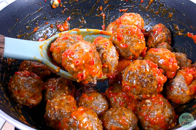 A large spoon is scooping keto meatballs tossed in a spicy garlic sauce.