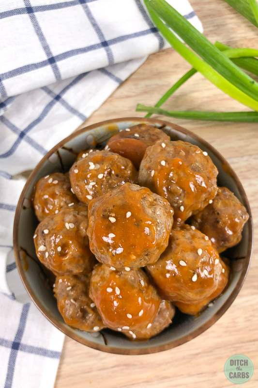 Bowl of keto sweet and sour meatballs topped with white sesame seeds.