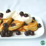 blueberry paleo pancakes on a white plate with whipped cream and berries