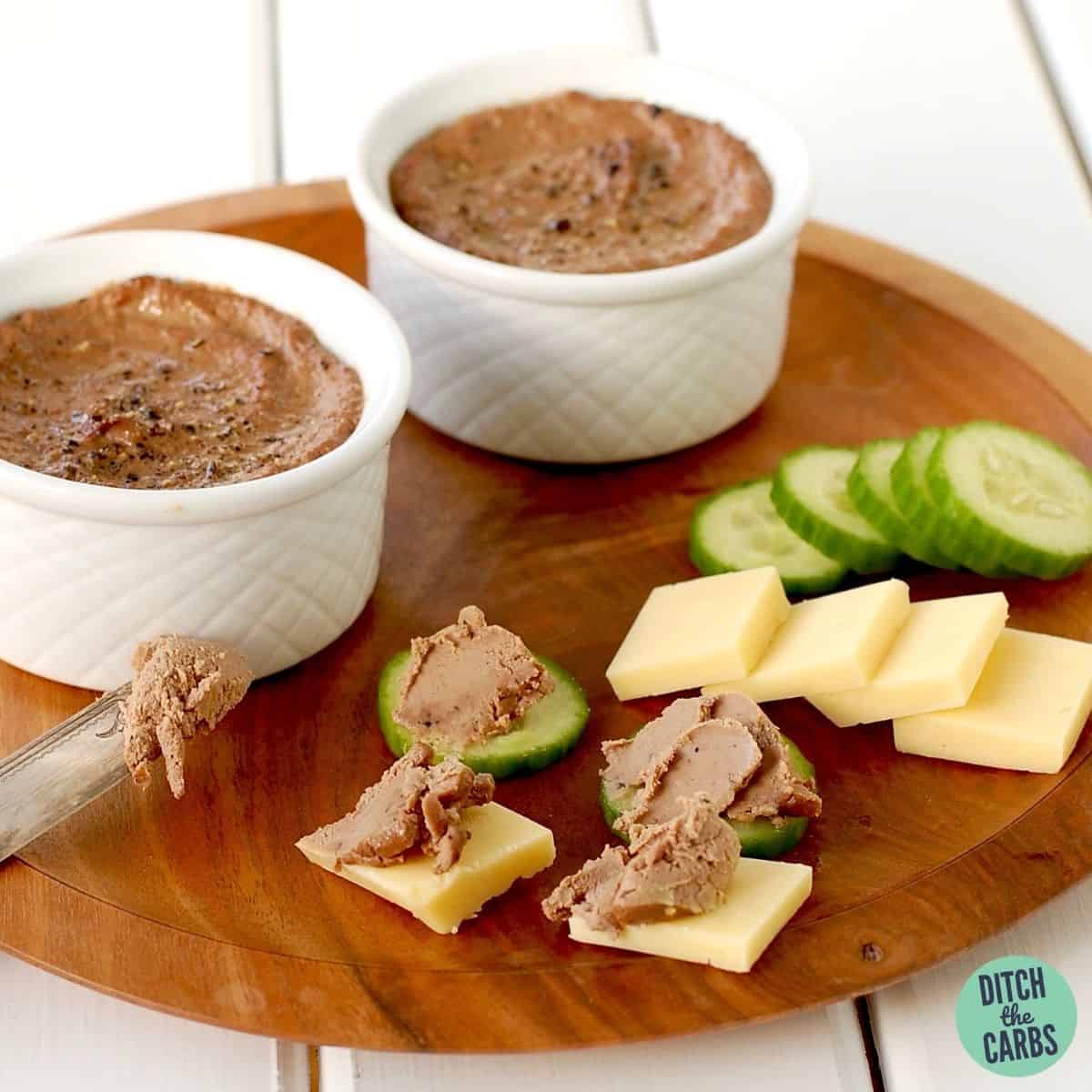 A wooden serving plate with homemade garlic pate, slices of cheese and slices of cucumber