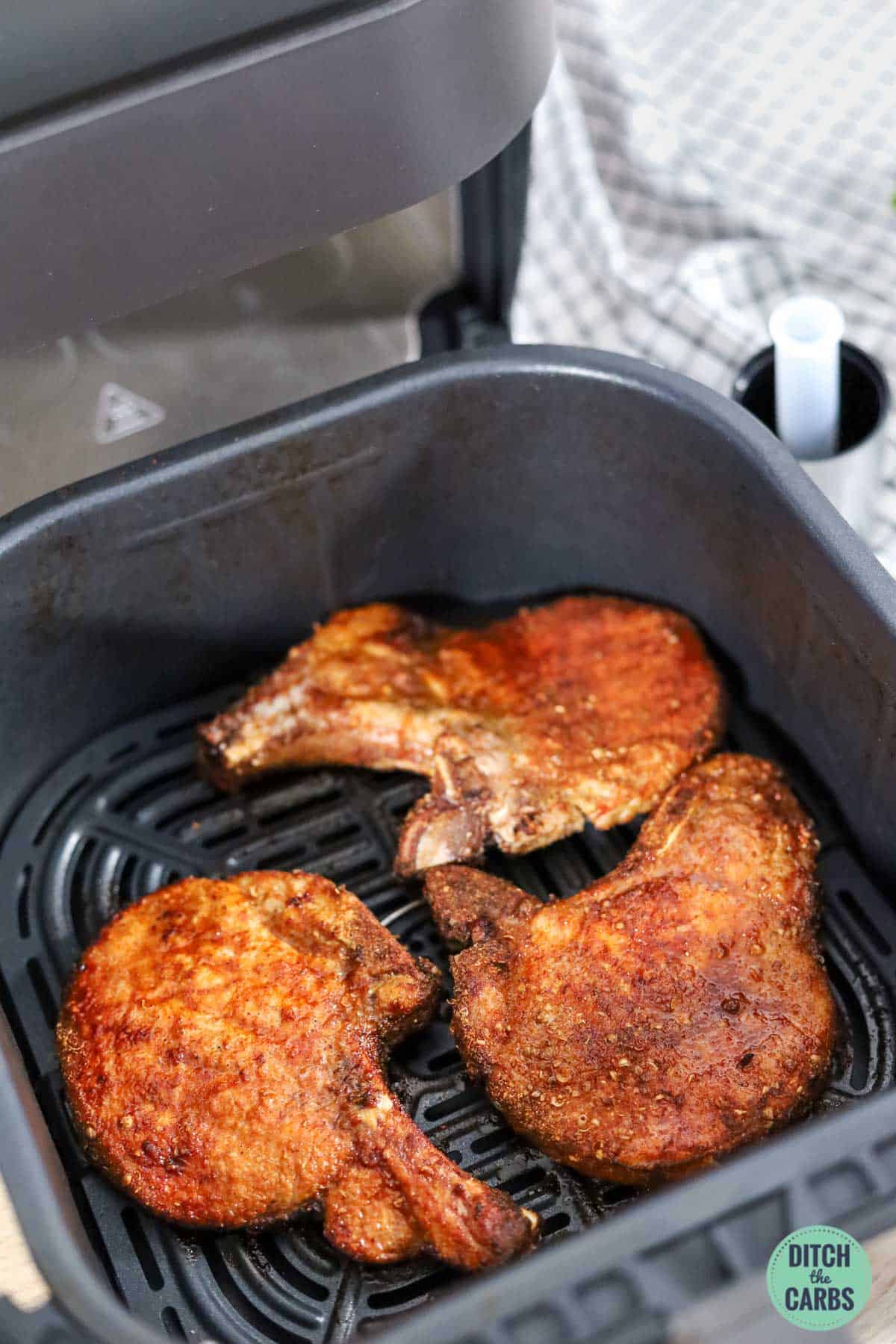 Air fryer basket with bone-in pork chops cooking