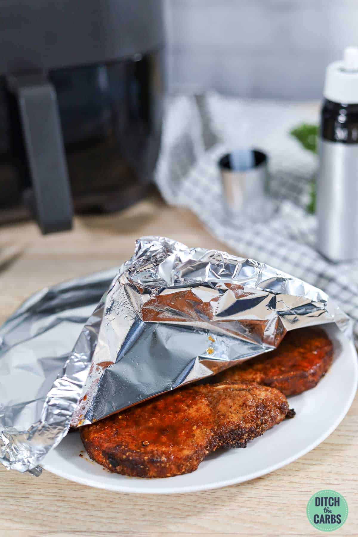 Cooked pork chops resting under aluminum foil