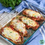 Four keto chicken parmesan baked in a clean glass baking pan resting on the counter.