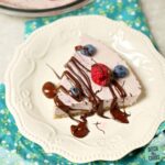 low-carb no bake blueberry cheesecake served on a white dish and drizzled with sugar-free chocolate