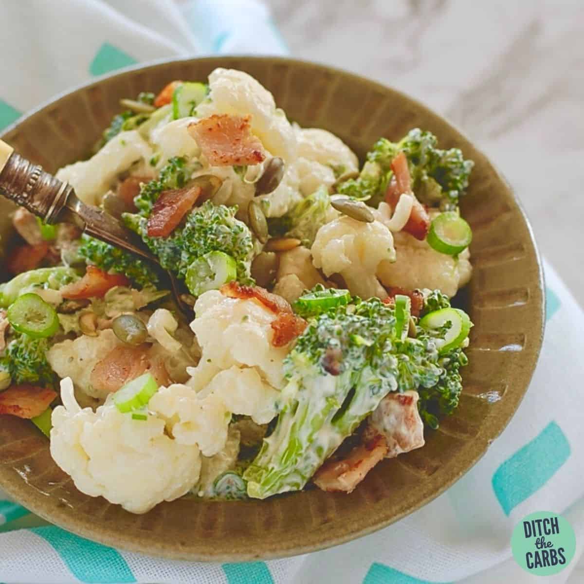 A green antique bowl of low-carb bacon broccoli cauliflower salad