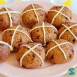 Cooked low carb hot Cross buns sitting on a fluted pink plate and a yellow and white cloth