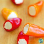 Mini peppers sliced in half and stuffed with cream cheese on a wooden chopping board