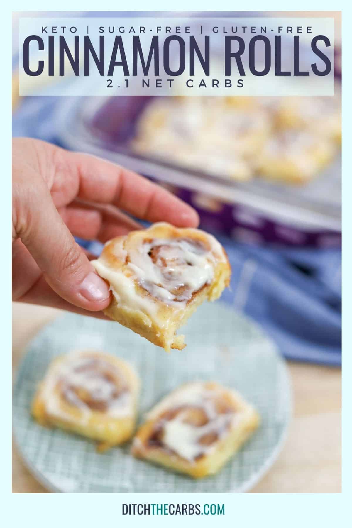 A hand lifting a keto cinnamon roll off a place with two more cinnamon rolls. The pan of rolls in the background.