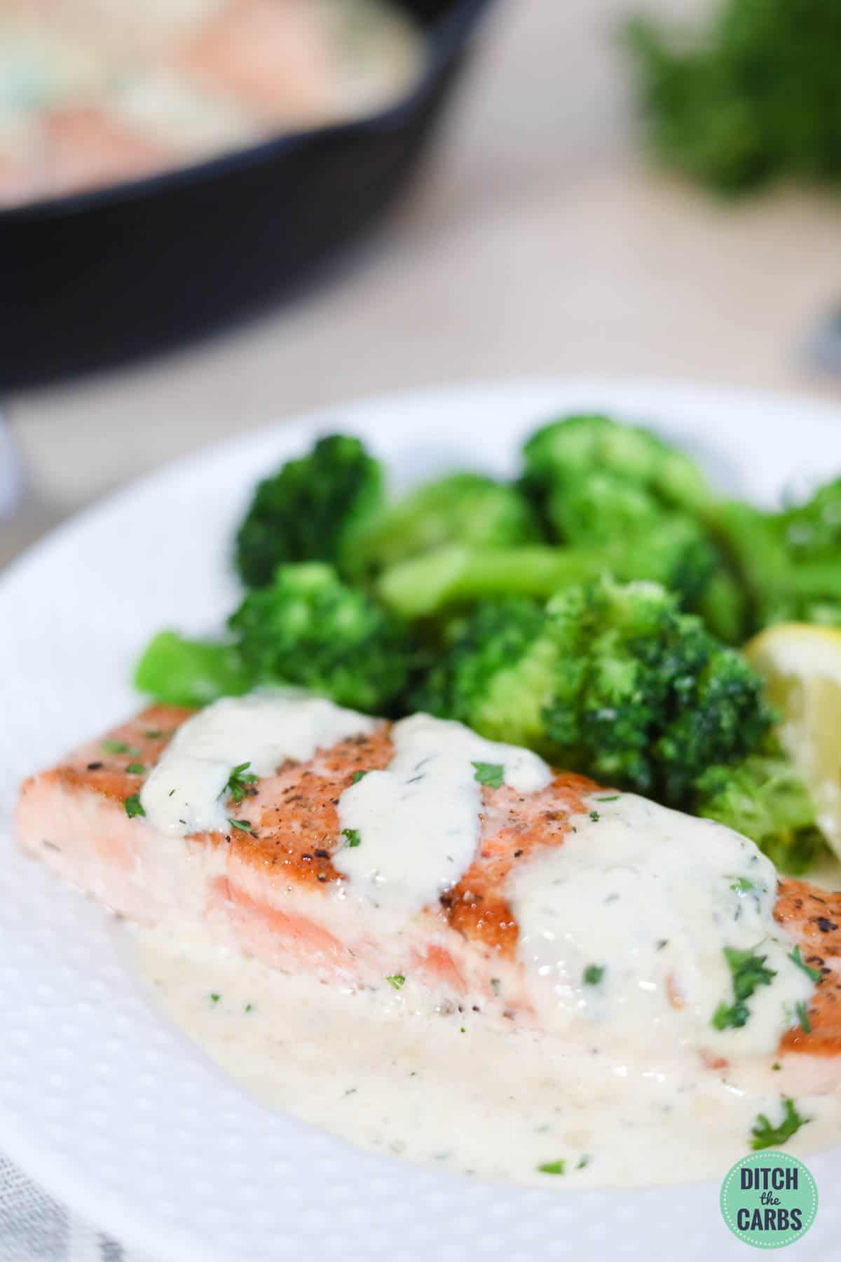 a white plate with cooked salmon fillet with garlic sauce drizzled over the top