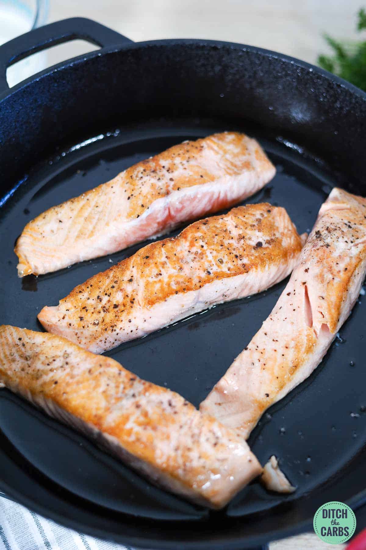 four salmon fillets skin side down being fried
