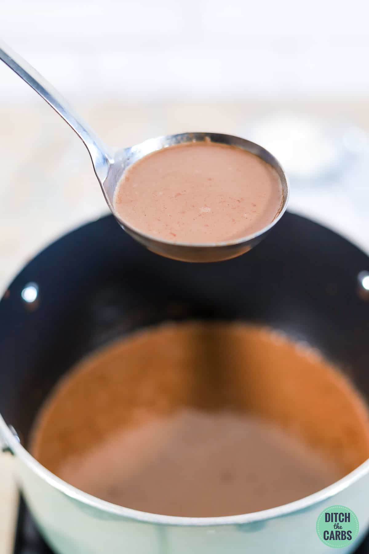 a ladle scooping a spoonful of keto hot chocolate out of the pot