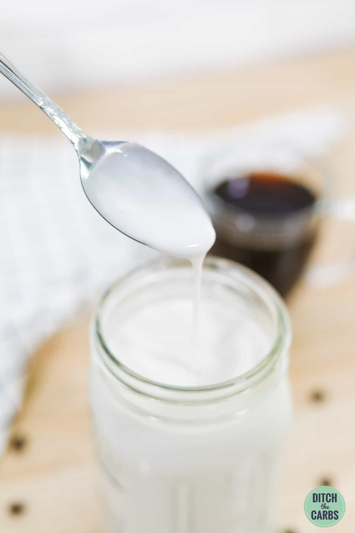 A spoon drizzling a spoonful of keto coffee creamer in a clear glass jar.