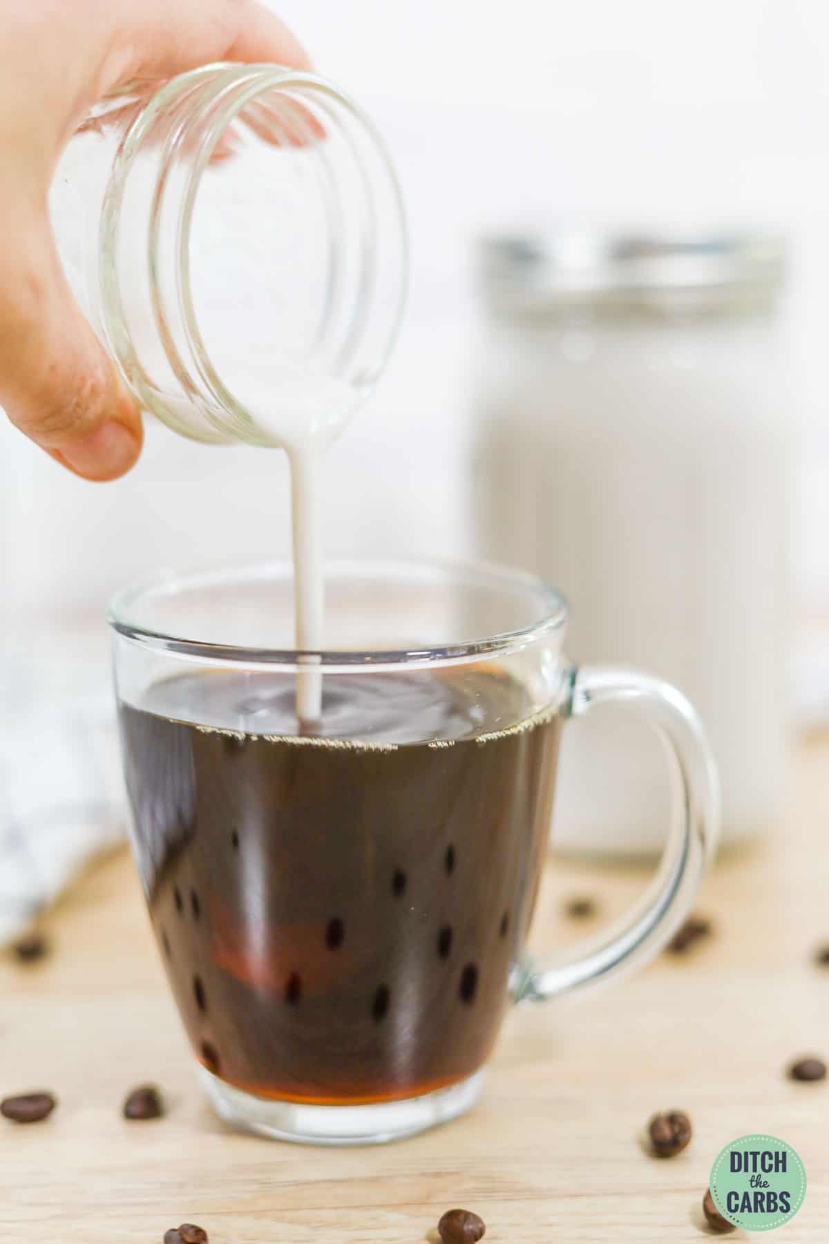 Keto coffee creamer being poured in a clear mug of coffee.