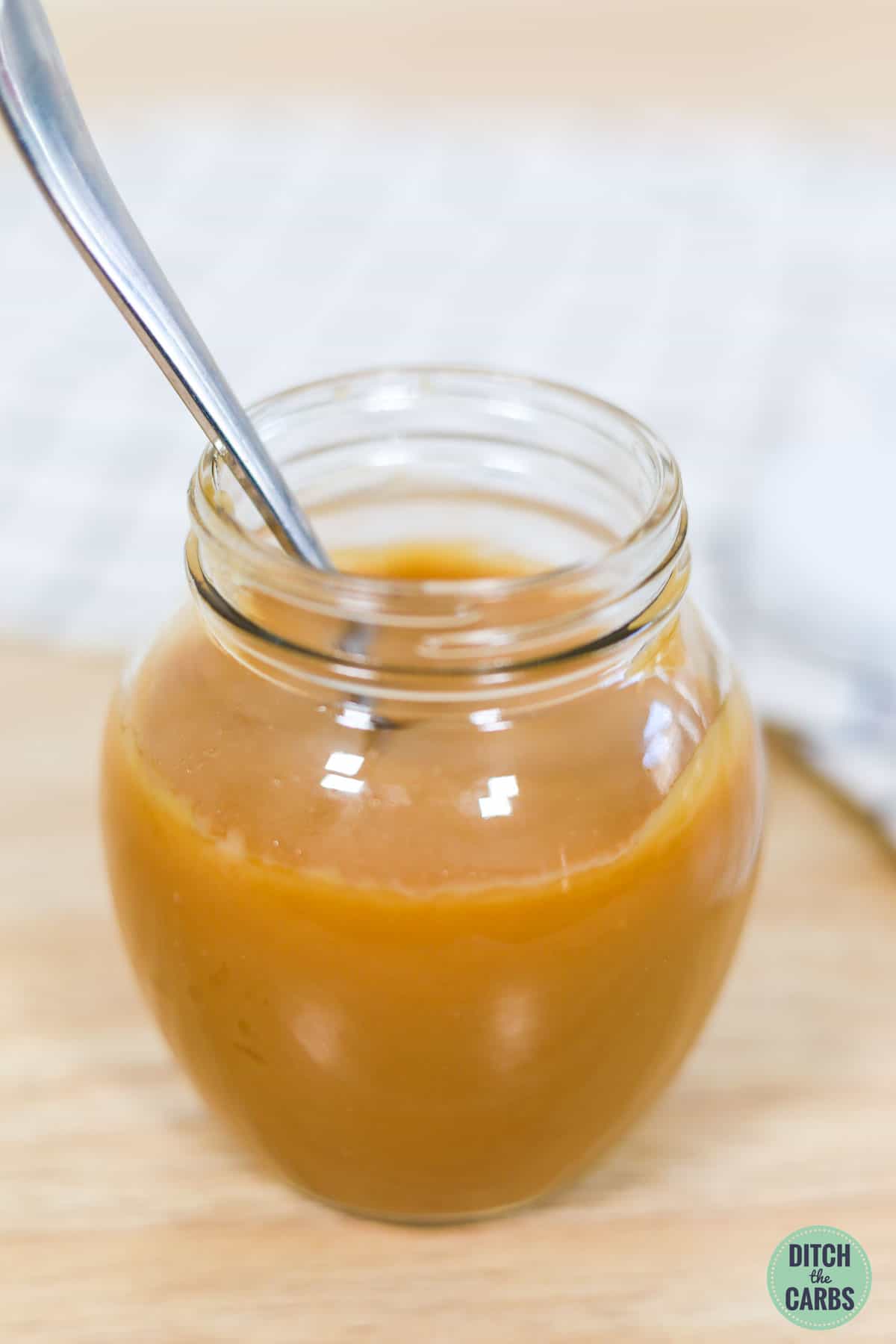 A jar of sugar-free keto caramel sauce with a spoon in it