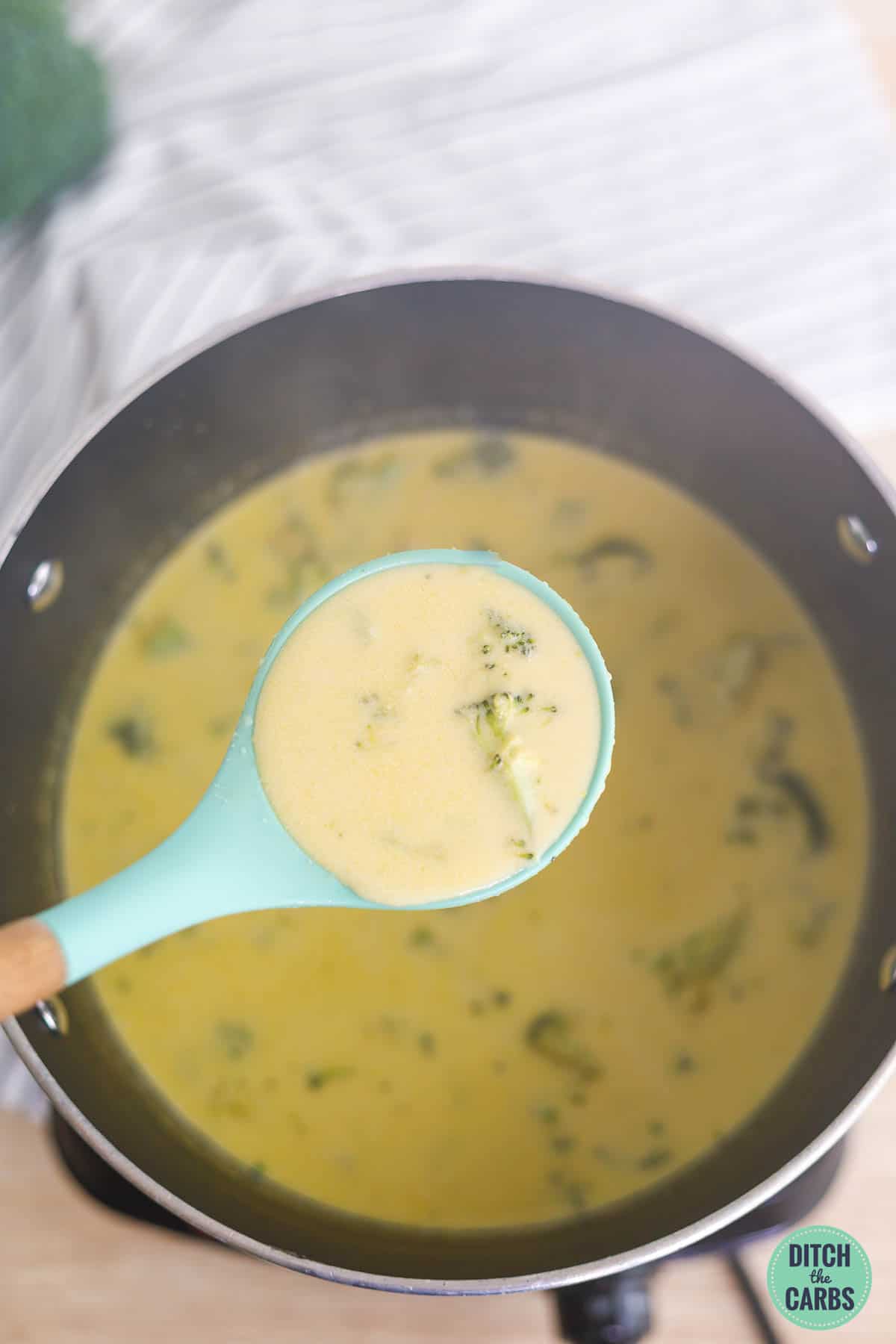 spoonful of keto broccoli cheese soup held over a pot full