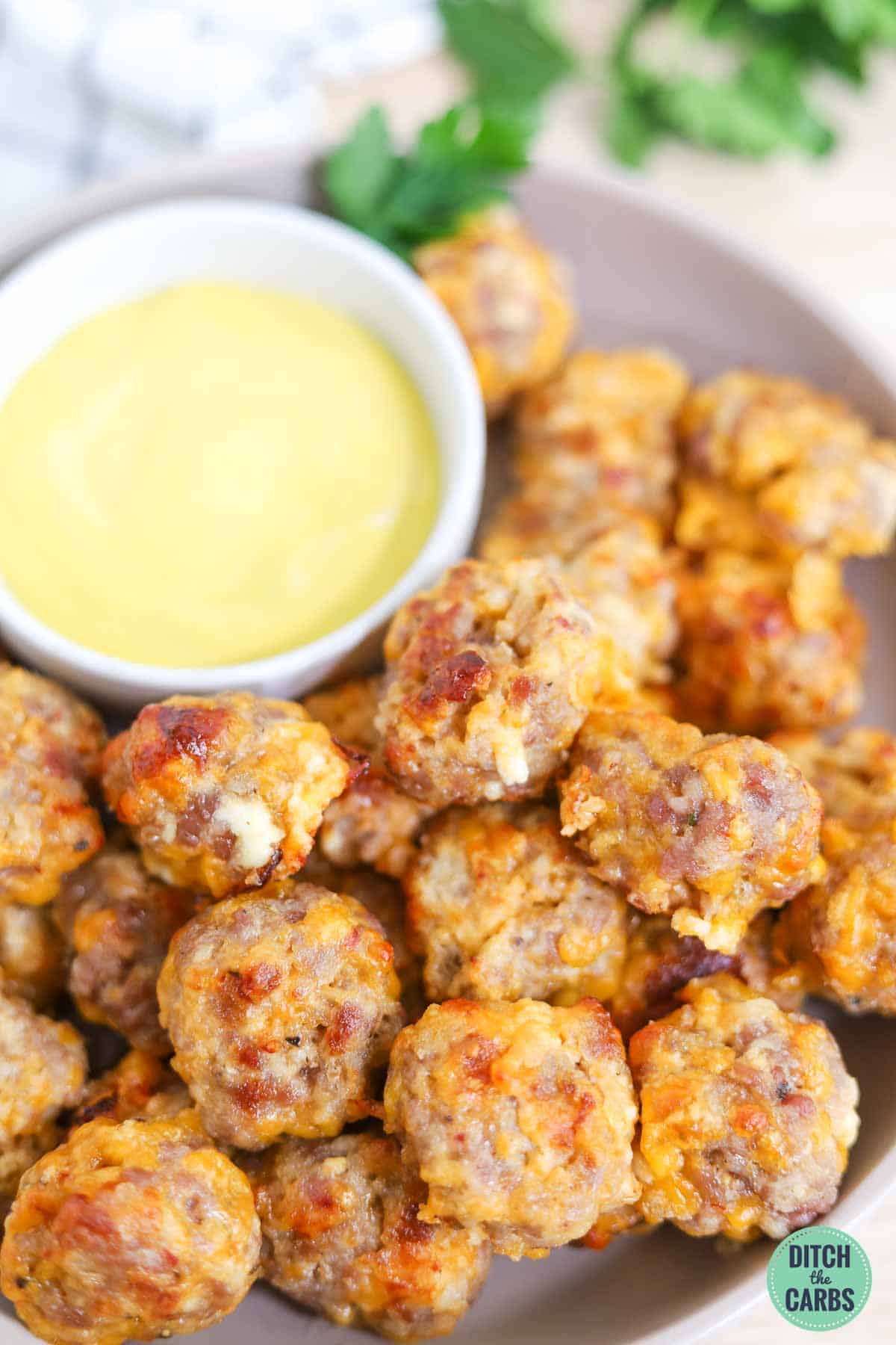 golden brown keto sausage balls on a platter with a bowl of dipping sauce