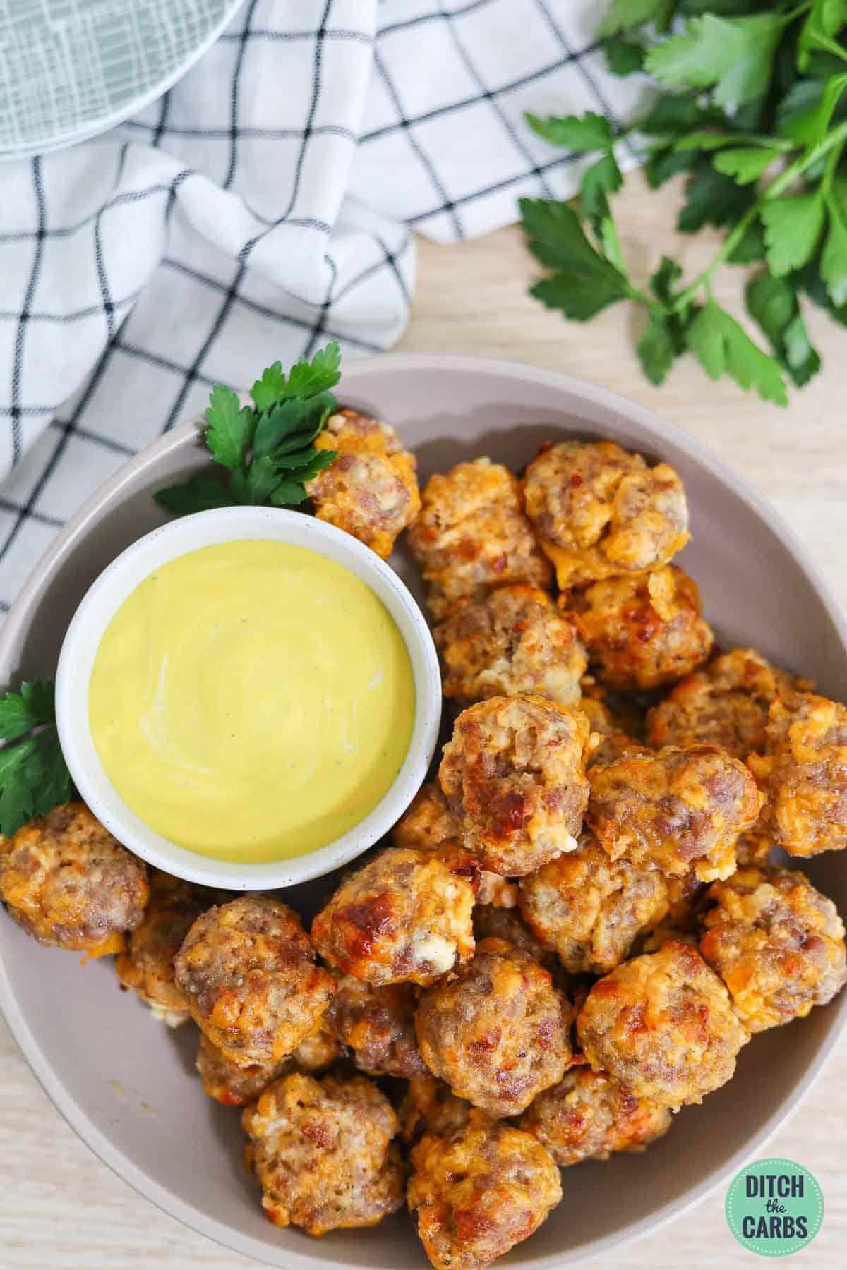 Keto sausage balls on a round serving plate with a side of mustard.