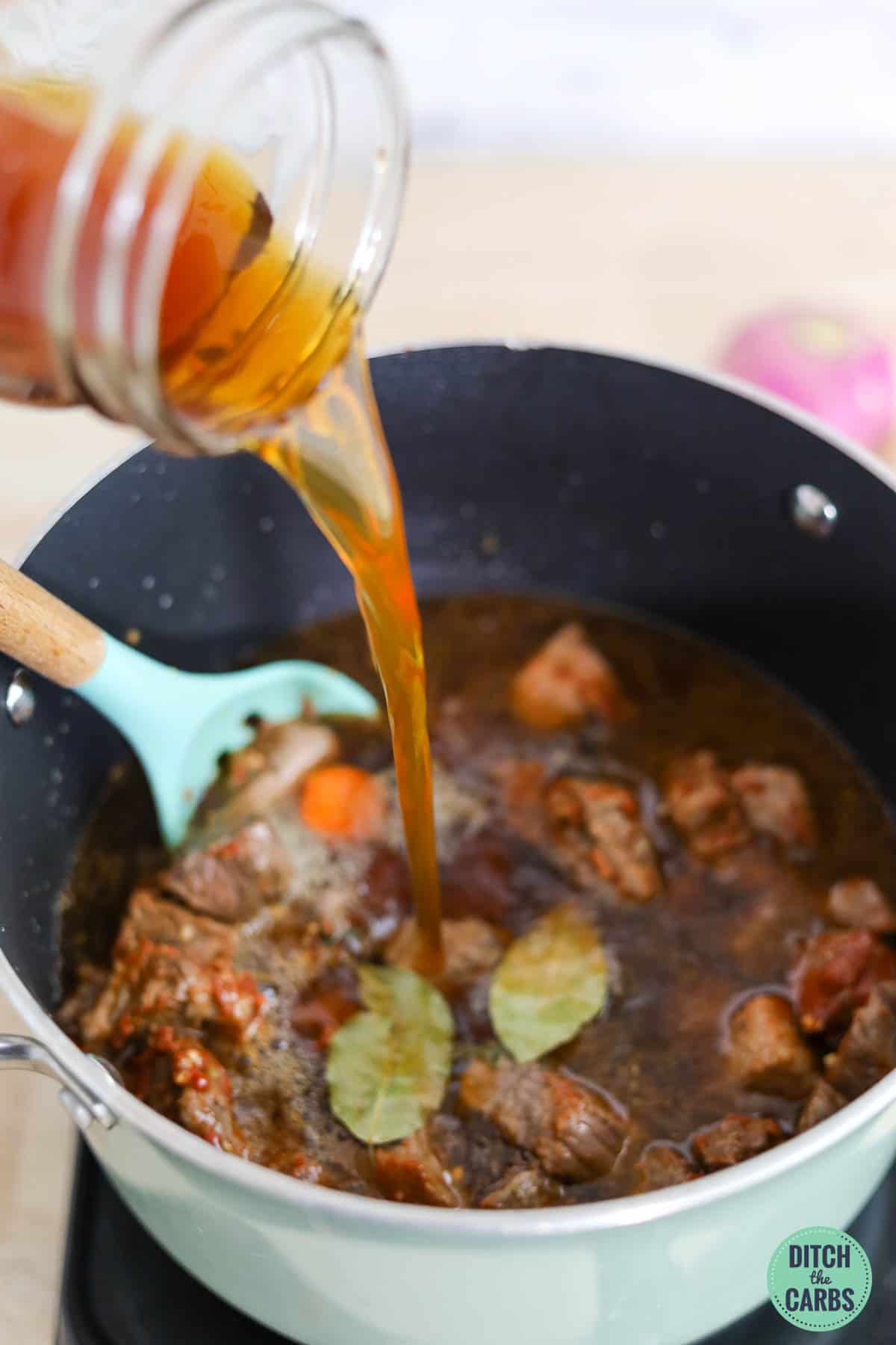 pouring beef broth into keto stew
