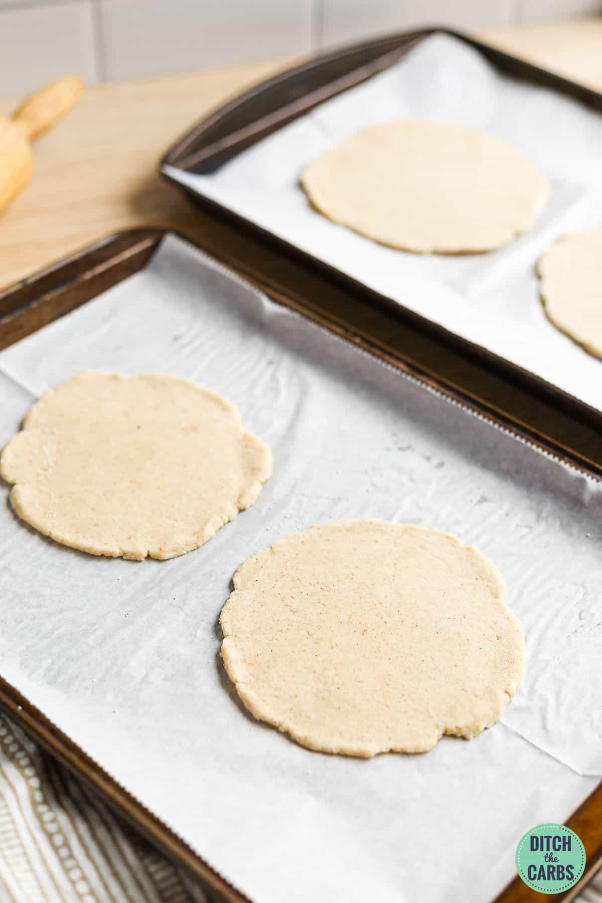 4 uncooked pita on baking sheets lined with parchment paper ready to cook.