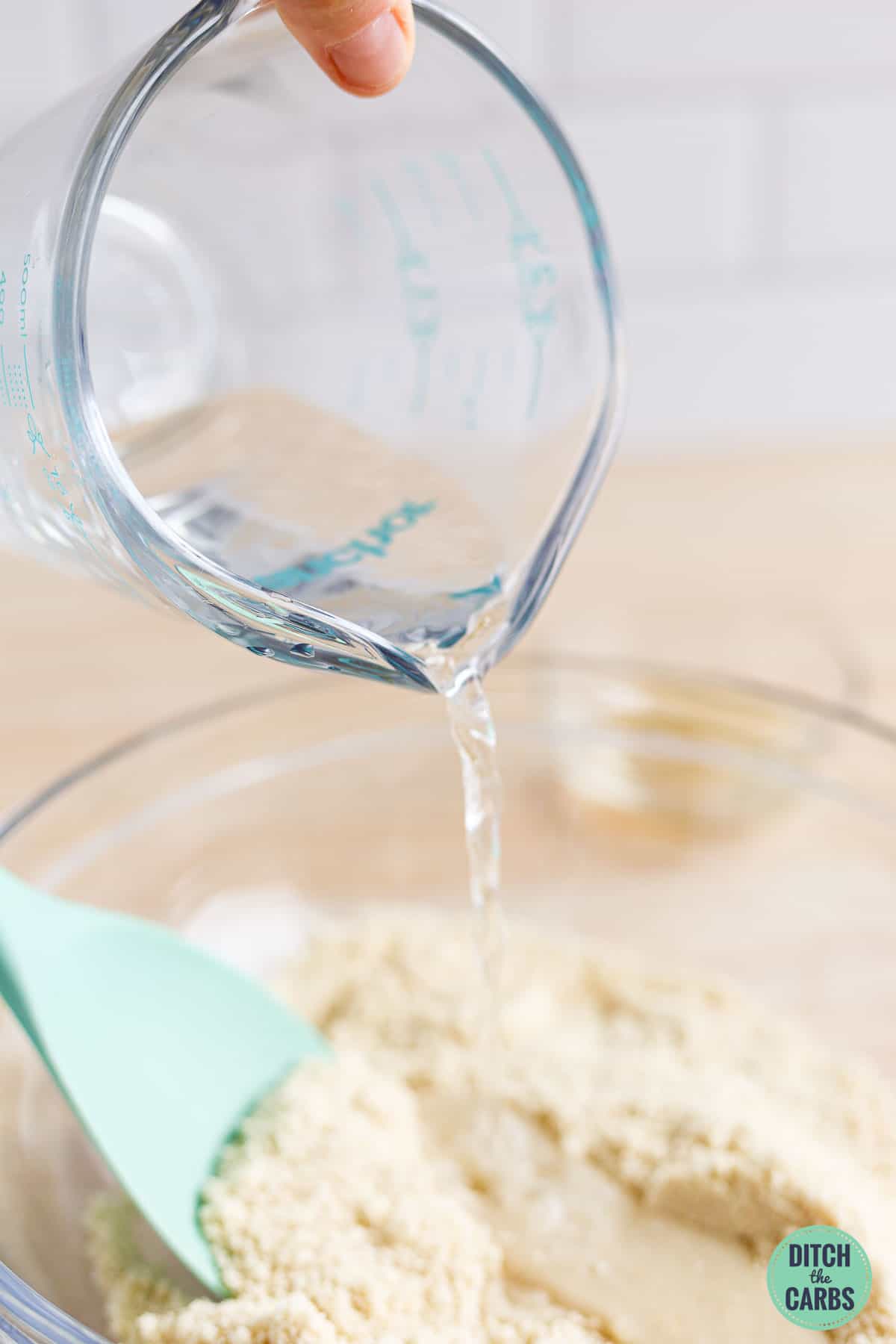Pour water into a bowl to mix together low-carb pita bread dough.