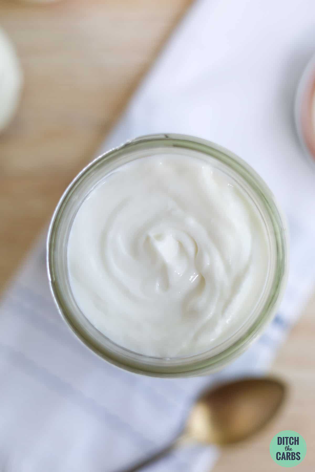 Overhead image of low-carb Greek yogurt in a glass jar resting on a towel.