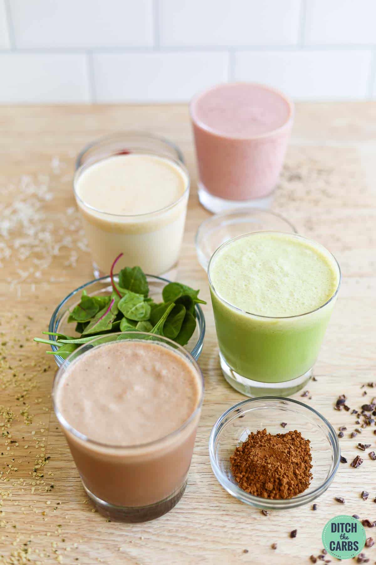 4 variations of low-carb protein shakes in glass cups with a bowl of the variation ingredients next to it.