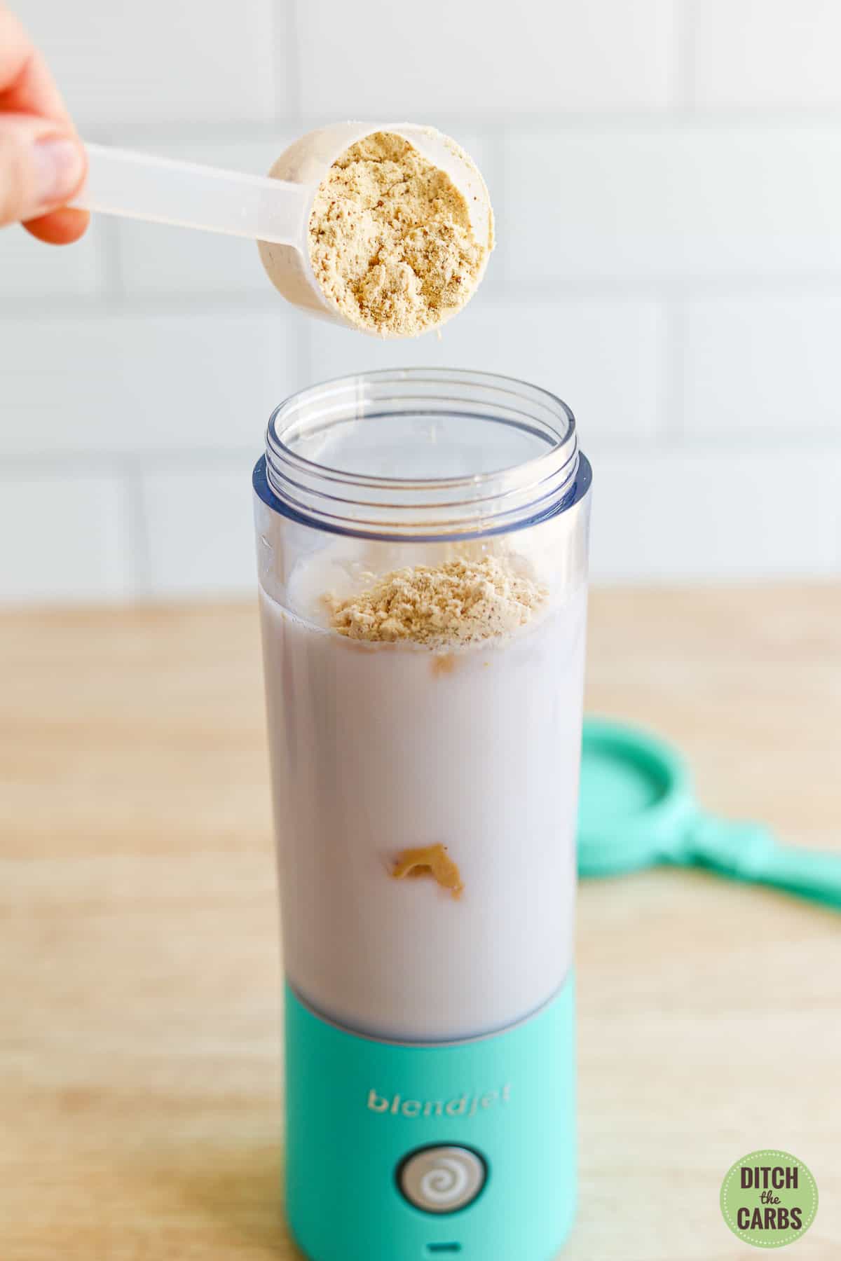 A had is adding a scoop of protein powder to the low-carb protein shake in a personalized blender.